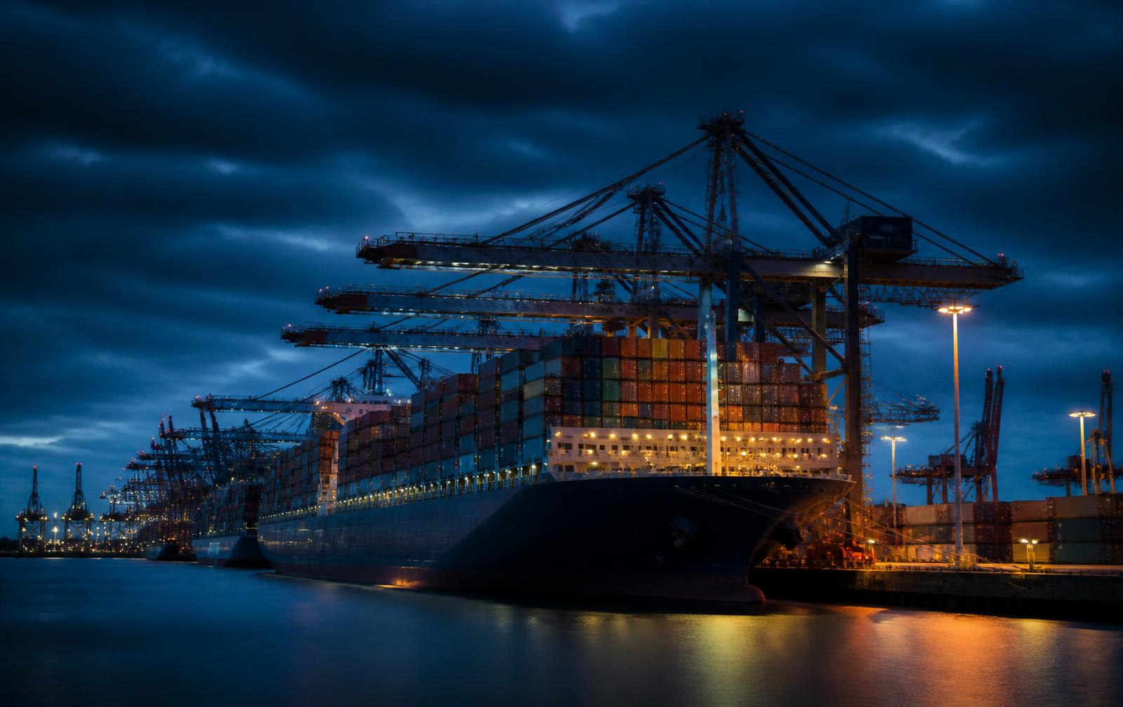 Container ship berthed under gantry cranes at a global port at dusk